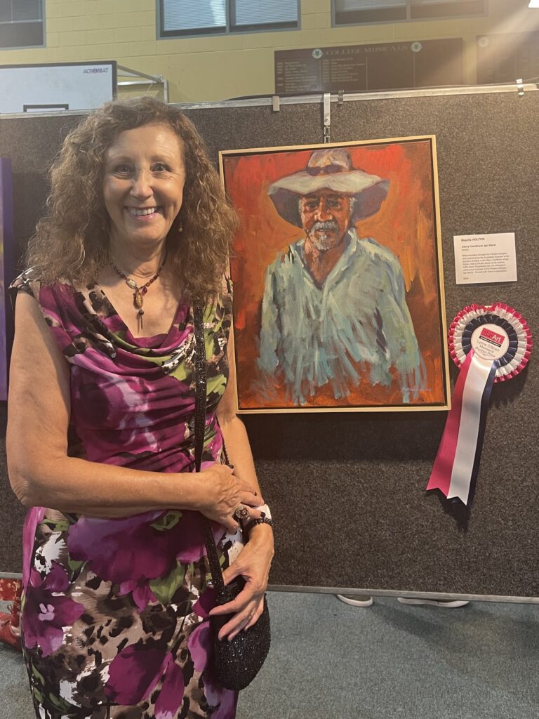 Artist standing beside her winning Portrait with a vibrant orange background