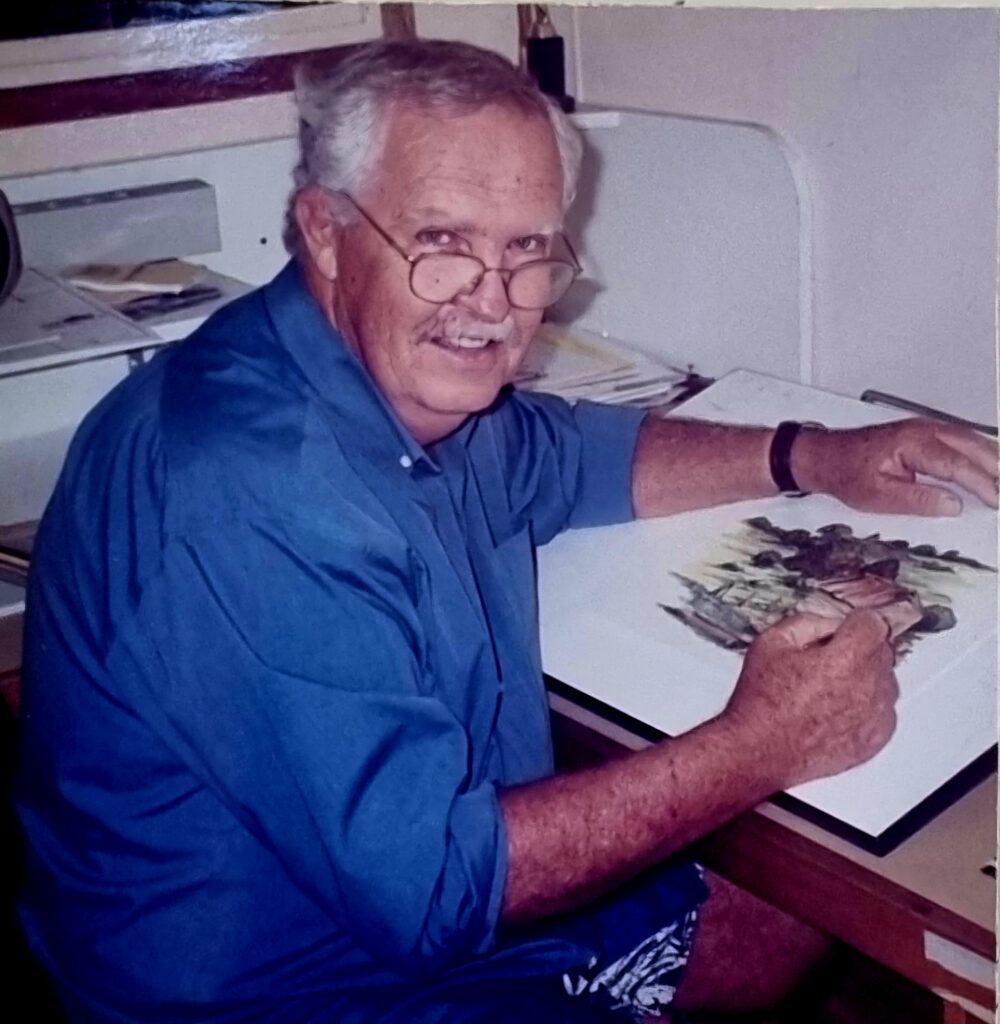 man in a blue shirt sitting at his drawing desk