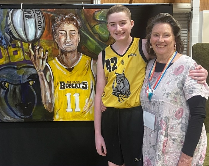 Artist Jill Lincoln standing near a colourful painting of a young basketballer with a yellow top